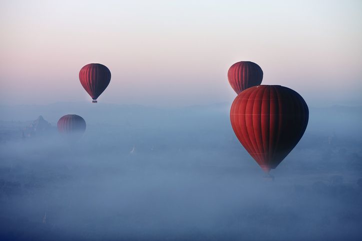 Several red air baloons flying in a misty sky. 
