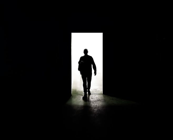 Mysterious man walking through door in between darkness and light - stock photo