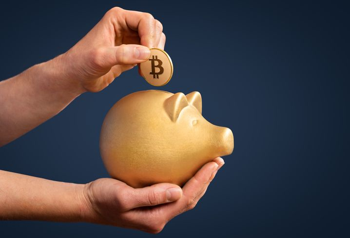 A stock photo featuring a woman inserting Bitcoin coin in a golden piggy bank.