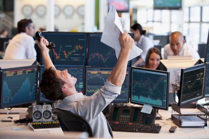 A stock photo of a trader cheering in front of the monitors with candle charts. 