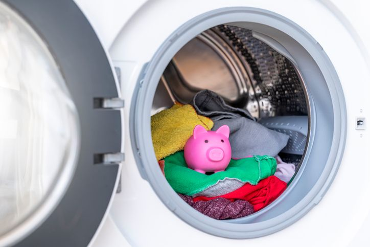 A stock photo of a washing machine with clothes and a piggy bank inside.