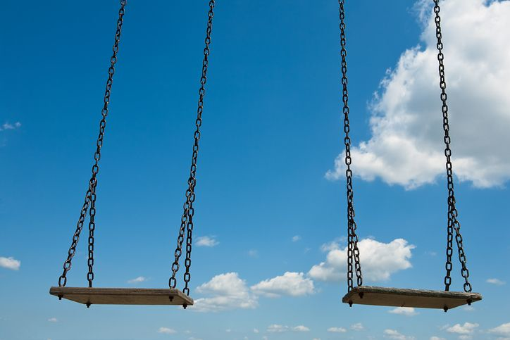 Stock photo of two empty swings against blue summer sky