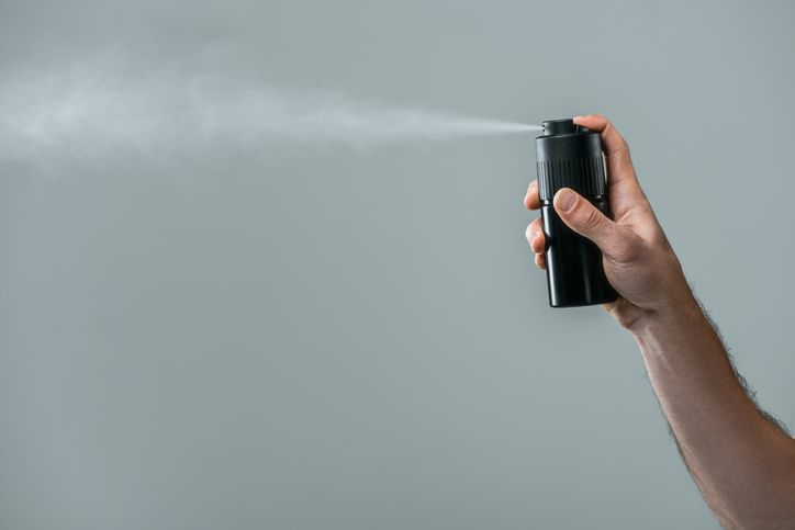 A stock photo of cropped man's hand spraying deodorant from the black can.
