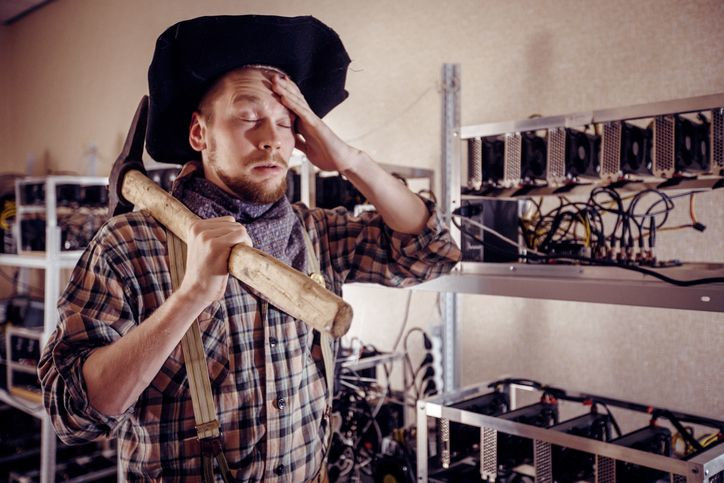 A stock image of the tired coal miner in front of the crypto mining rig. 