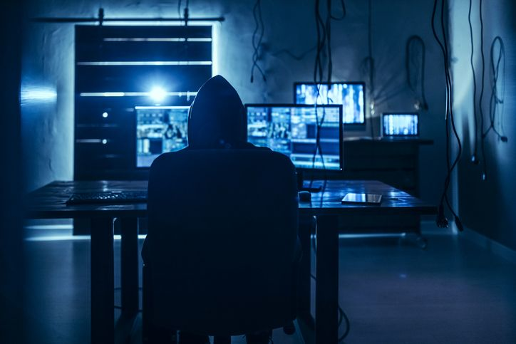 Hooded hacker in a dimly lit room