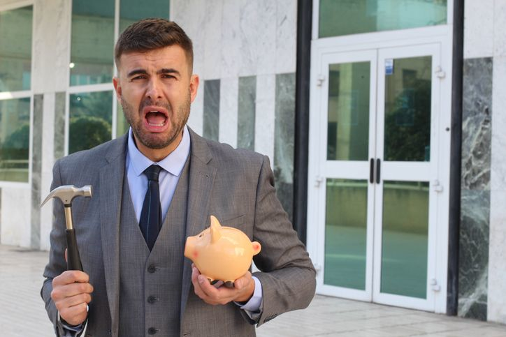 A stock image of businessman about to break piggy bank with hammer.