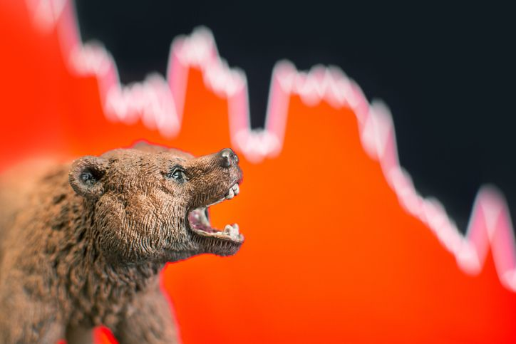 A stock photo featuring a bear figure in front of red price down chart.