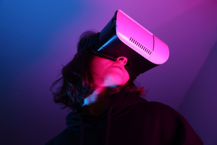 A stock photo of a woman wearing VR goggles in neon light. 