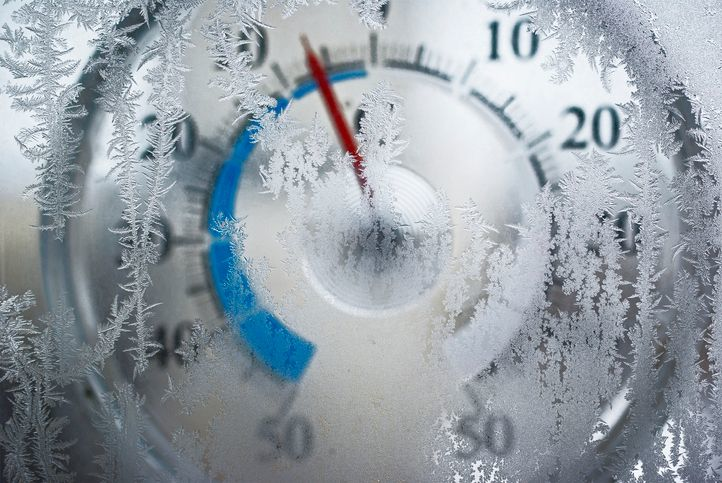 Round thermometer showing below zero temperatures behind frosty glass