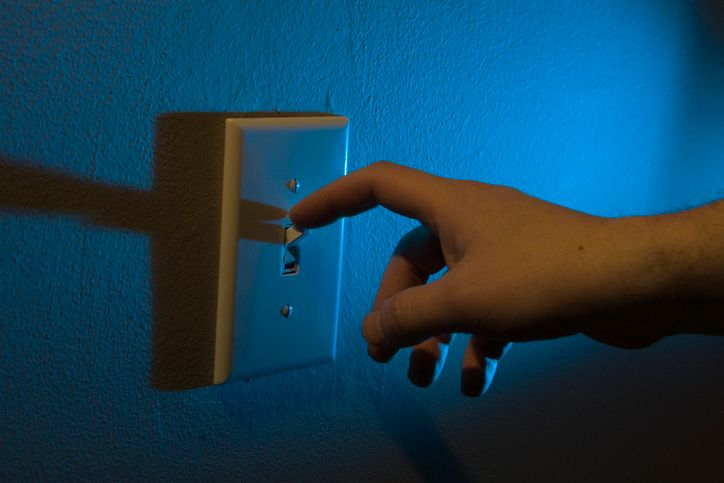 A stock photo featuring male hand turning off the lights at night.