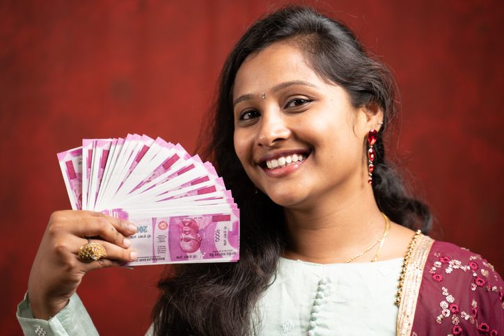 A stock photo of a smiling Indian girl holding rupee banknotes. 
