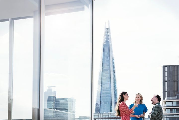 Three people talking cheerfully on a terrace with London skyscrapers behind them