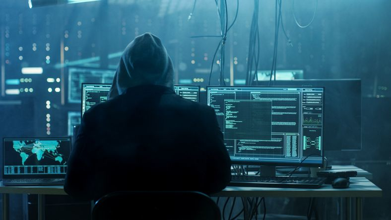 A male hacker wearing a hooded jacket works on the computer.