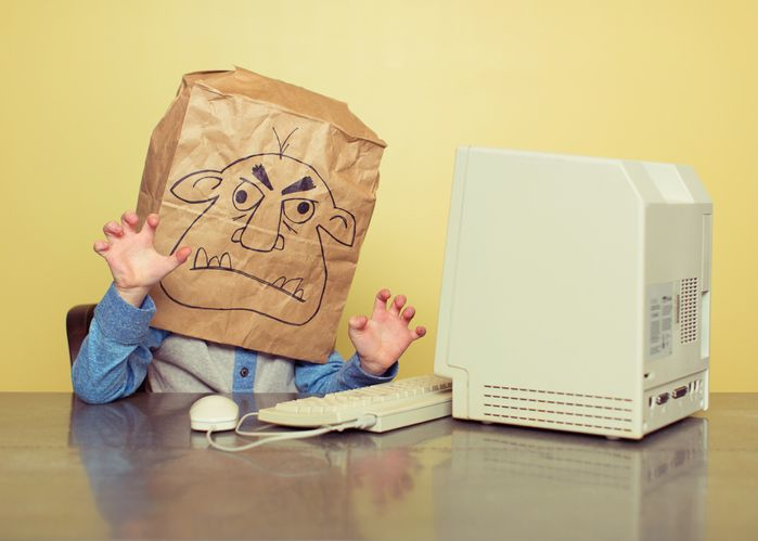 A stock photo of an internet troll hiding behind the paper bag in front of the computer. 