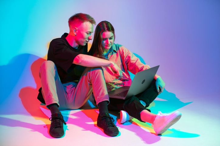 A stock photo of a young couple in neon lights looking at the laptop screen. 