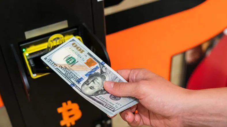Hand holding dollars over Bitcoin ATM's slot 