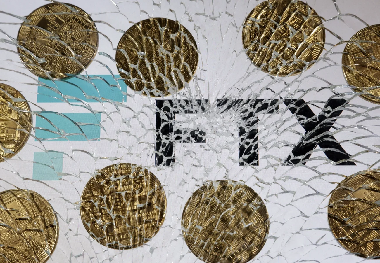 An FTX logo and a representation of cryptocurrencies are seen through broken glass 