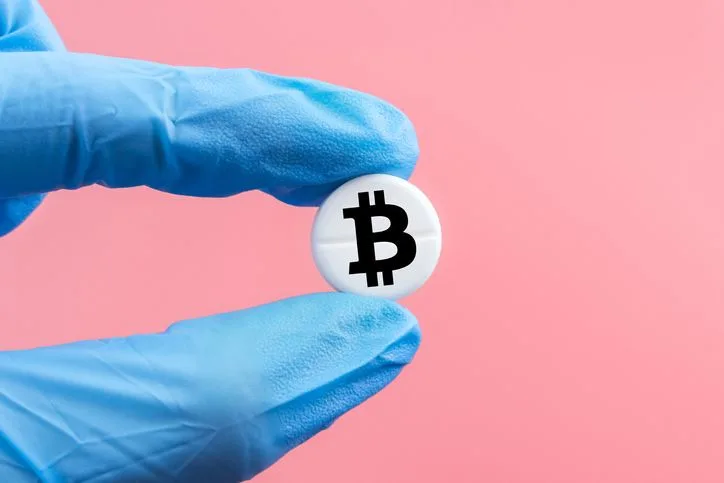 Medical pill with a bitcoin sign in a hand in a medical glove on a pink background. Bitcoin technology concept in medicine - stock photo