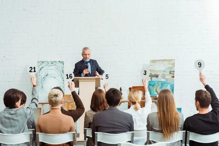 Auctioneer talking with microphone and looking at buyers with auction paddles during auction - stock photo