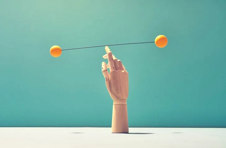 A  stock photo featuring wooden hand balancing two spheres on one finger.