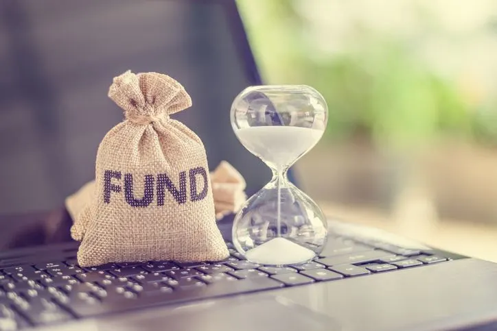 A stock photo of an hourglass and a bag of money on top of the laptop keyboard. 