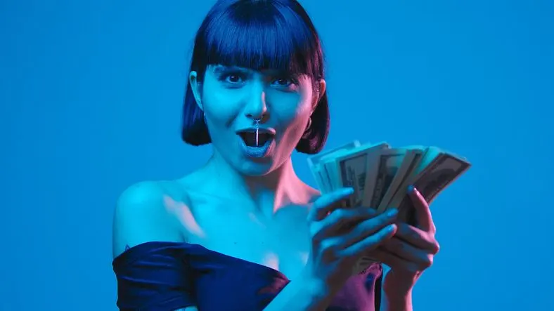 A stock photo of an excited woman holding a wad of cash.