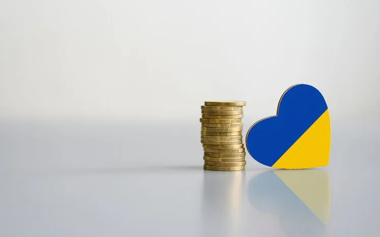 A stock photo of a pile of coins and a heart in colours of Ukrainian flag. 