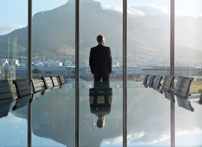 A stock photo featuring male CEO looking at the rising sun from the window.