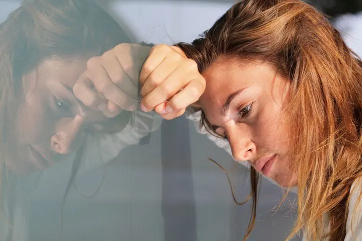 A stock image featuring a concerned woman leaning on the glass wall. 