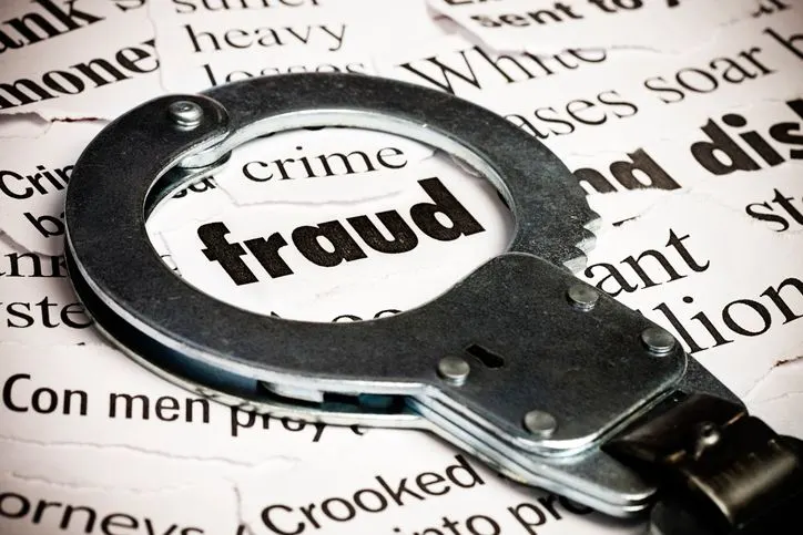 Handcuffs over newspaper with the word fraud - stock photo