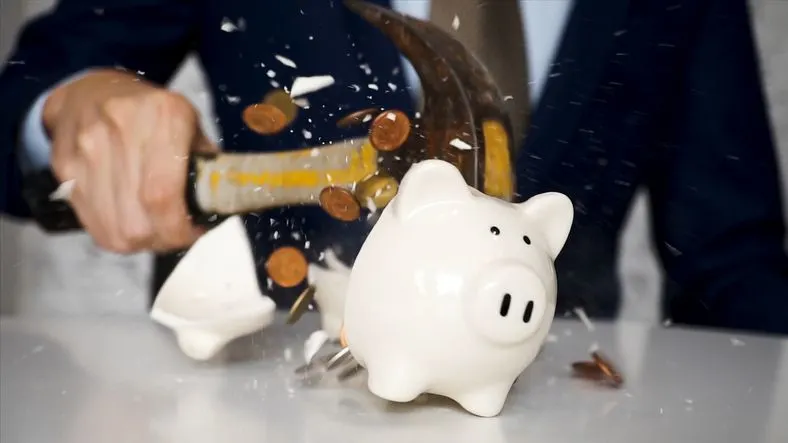 Close-up of businessman using a hammer to smash plenty of coins inside piggybank