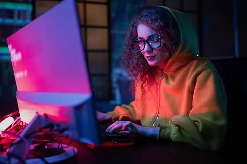 Young hacker woman working on computer at dark place. 