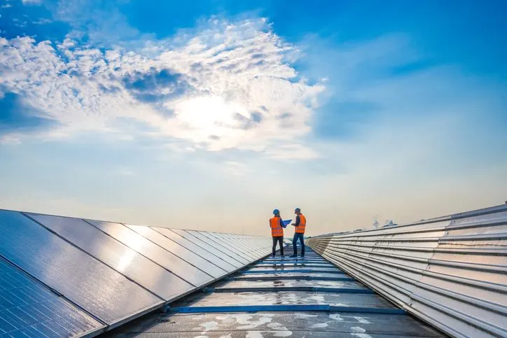 A stock photo of the rows of solar panels and to technicians in the distance. 