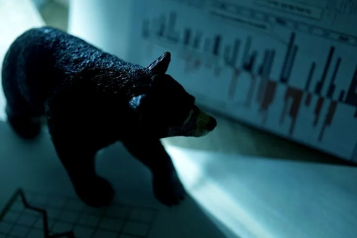A stock photo of a close-up bear figure with a financial chart in background. 