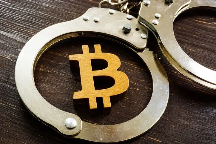 A stock photo featuring a golden Bitcoin sign inside the handcuffs. 