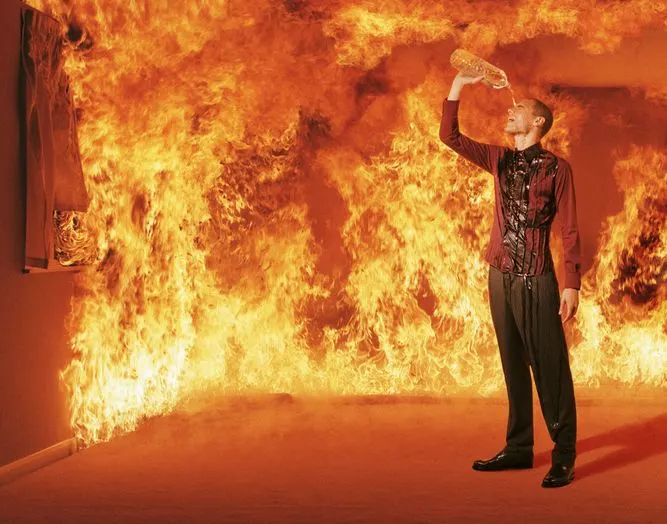 A stock photo of a man pouring water over his head in a burning building. 