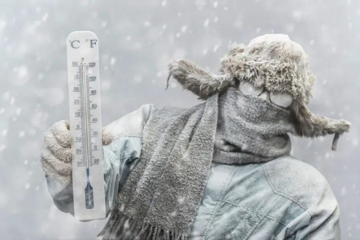 Frozen man holding a thermometer while it is snowing.