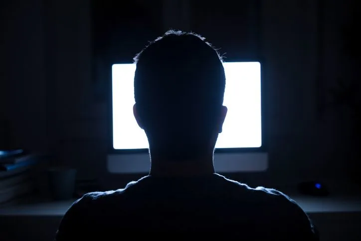 A stock photo of a man sitting in front of the bright monitor at night. 