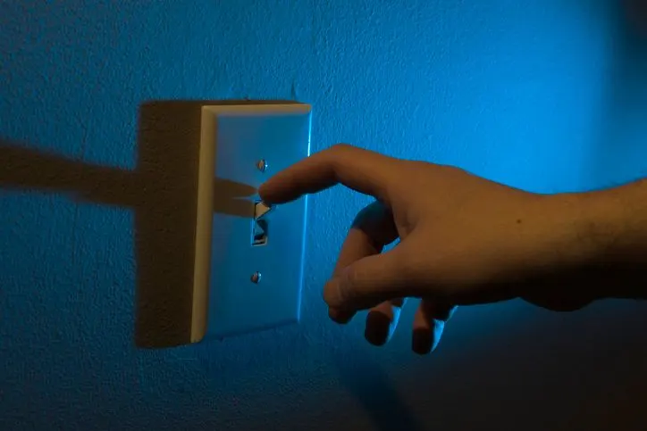 A stock photo featuring male hand turning off the lights at night.