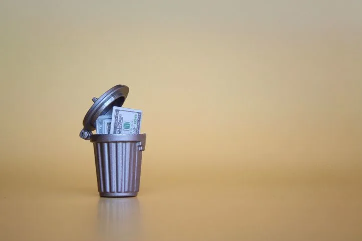 A stock photo of dollars in a trash can. 