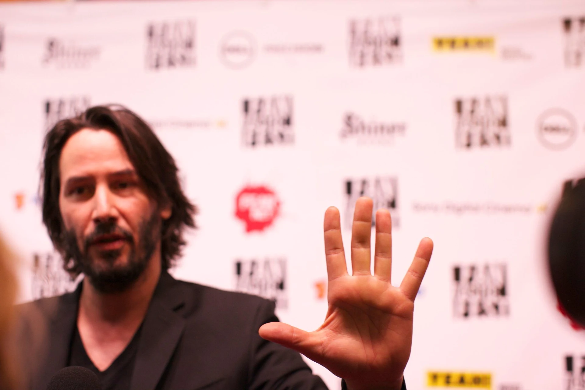 Keanu Reeves extending an open hand in a halting gesture to reporters at an event in 2013.
