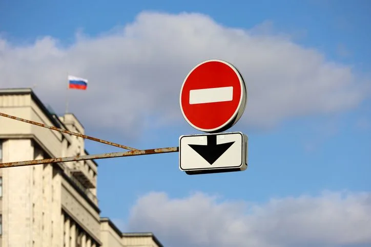 A stock photo of a stop road sign with a small Russian flag in background. 