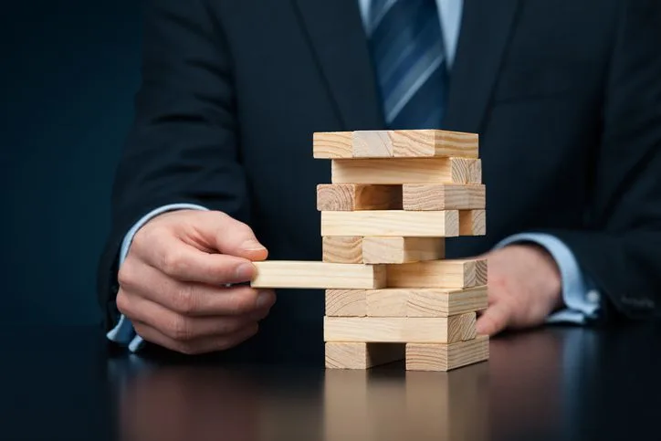 A stock photo featuring a businessman pulling one block from Jenga tower.