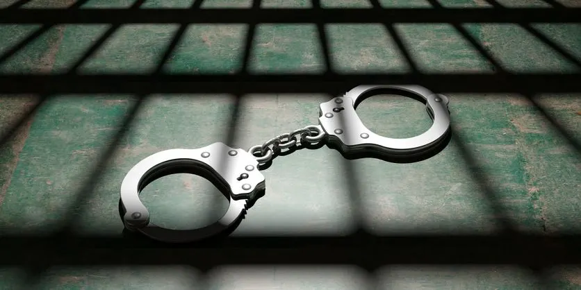 A stock photo of handcuffs behind the bars. 