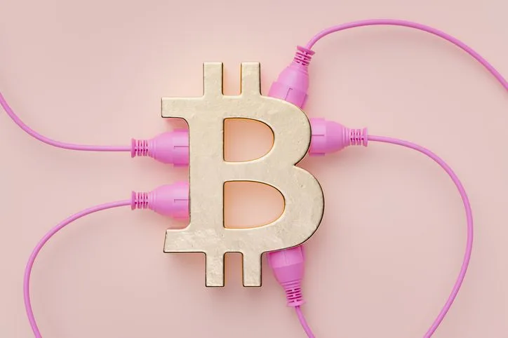 A stock image of a bitcoin logo with pink wires plugged in. 