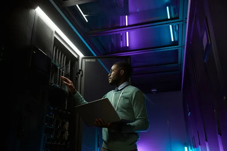A stock photo featuring a data centre technician with laptop checking on mining devices.