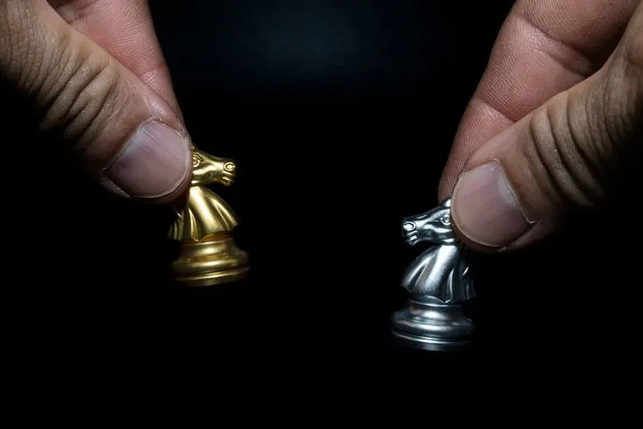 Close-up of a man holding a golden and silver chess horse - stock photo